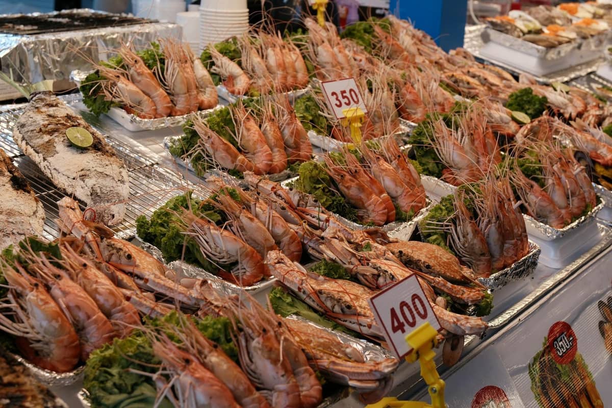 Display of grilled tiger prawns and seafood with price tags at a busy Pattaya market stall.