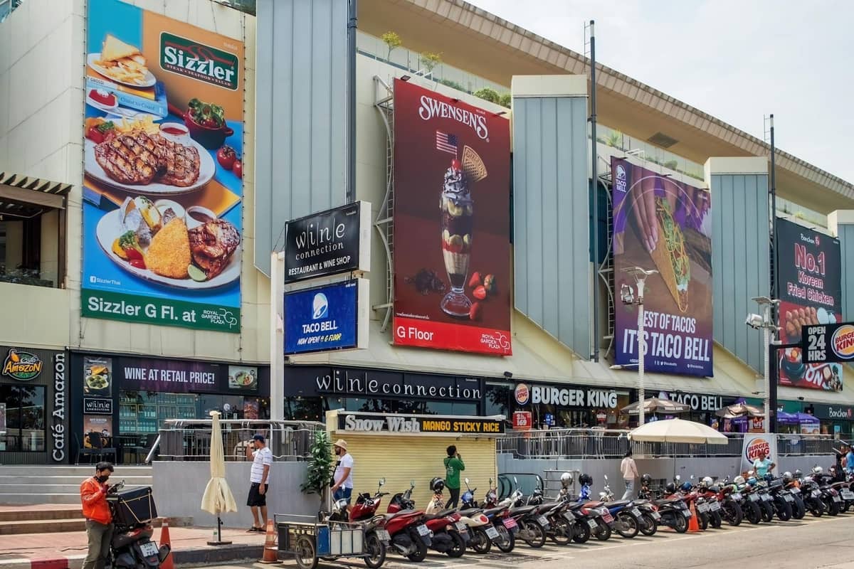Street view of a modern building in Pattaya with large signs for Sizzler, Swensen's, Burger King, and Taco Bell, showcasing international dining options.