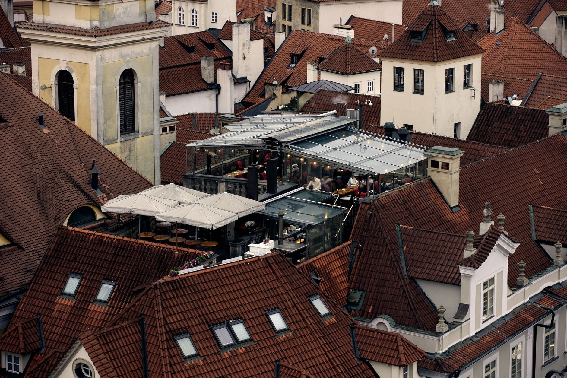 Ein Dachrestaurant inmitten der ikonischen roten Ziegeldächer von Prag, das modernes Dining mit historischer Stadtarchitektur verbindet.