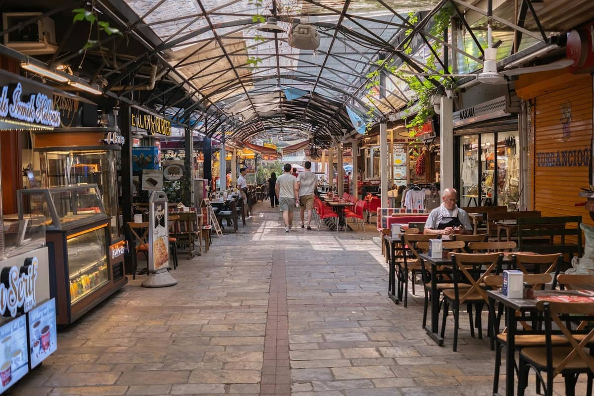 Covered alleyway lined with casual cafes and shops, people dining at simple tables, suggesting affordable local eateries.