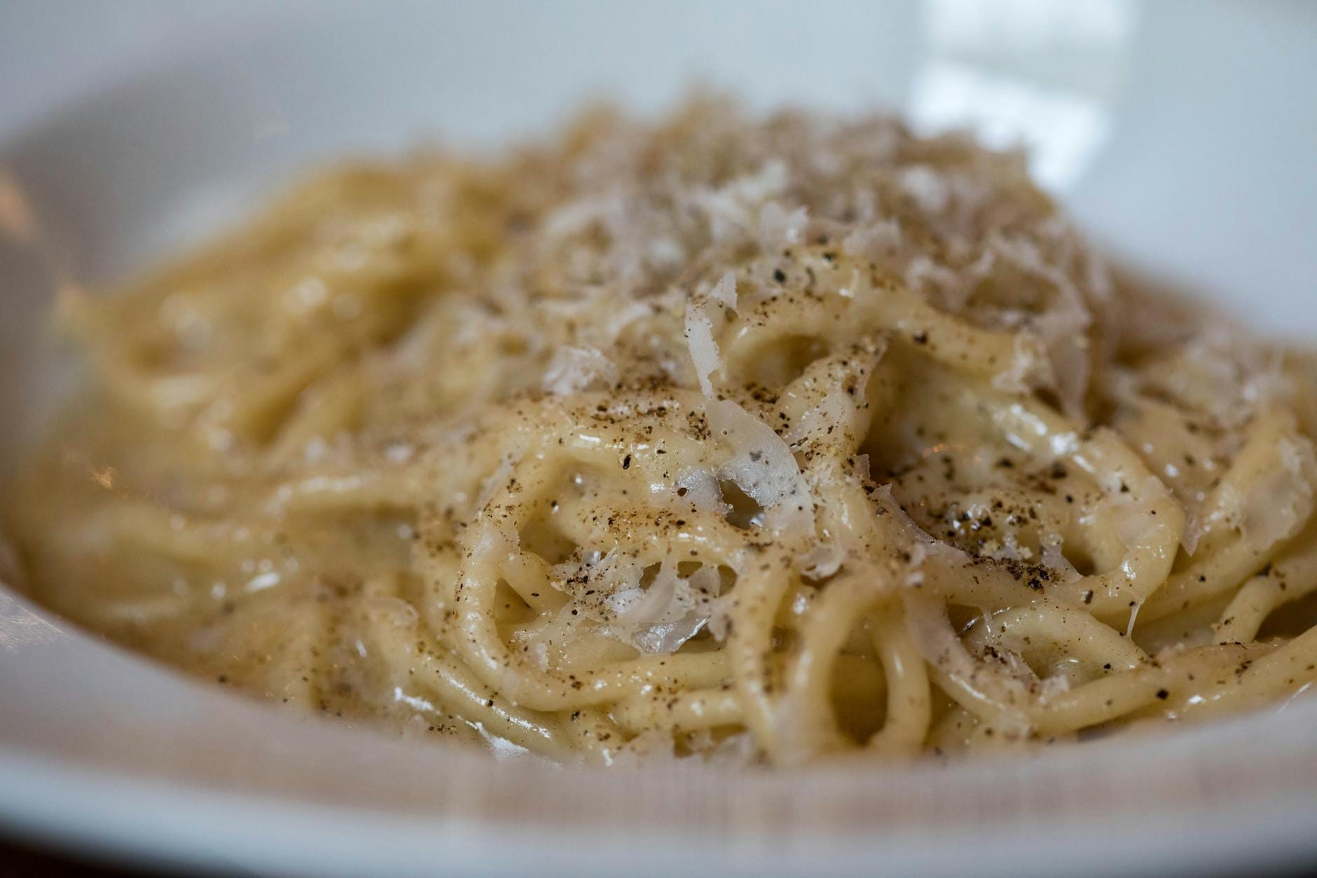 Close-up of a classic Roman pasta dish, cacio e pepe, garnished with black pepper and cheese in a white bowl.