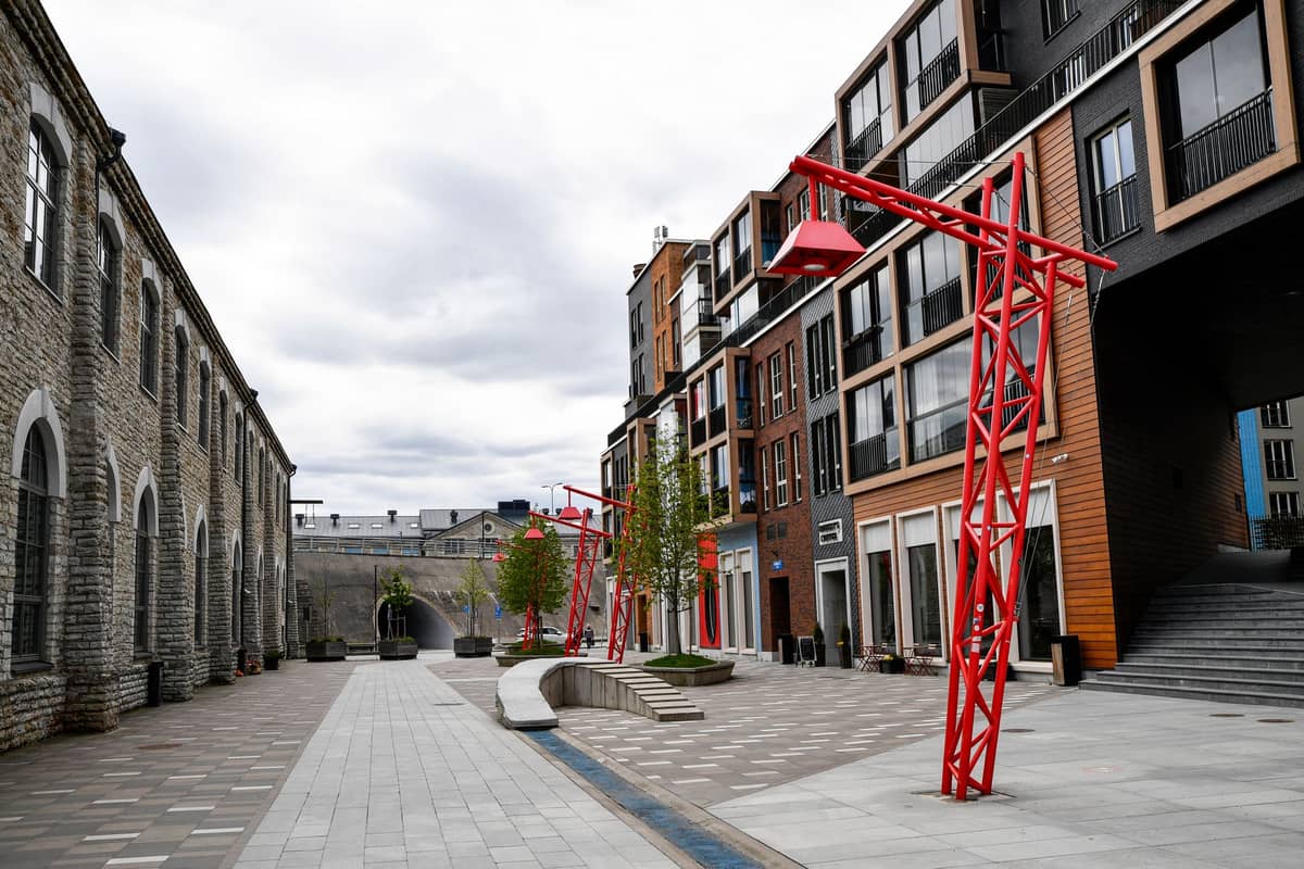 Moderne Stadtstraße mit Stein- und Holzgebäuden, roten Metallskulpturen und breitem Fußgängerbereich im neu gestalteten Viertel von Tallinn.