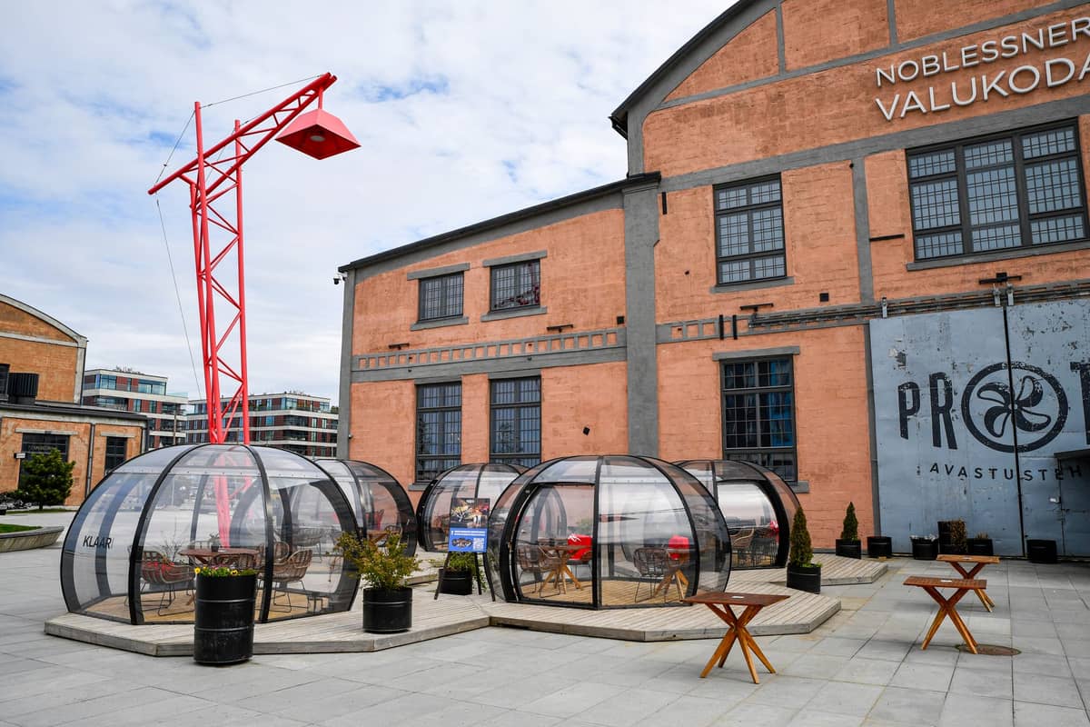 Outdoor-Dining-Kuppeln vor einem Backsteingebäude im Noblessner-Viertel von Tallinn, die die Anpassung an saisonale Speisemöglichkeiten zeigen.