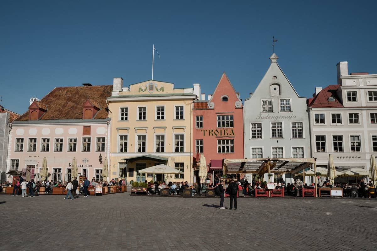 Tallinns Altstadtmarktplatz mit bunten historischen Gebäuden und belebter Außengastronomie unter blauem Himmel.