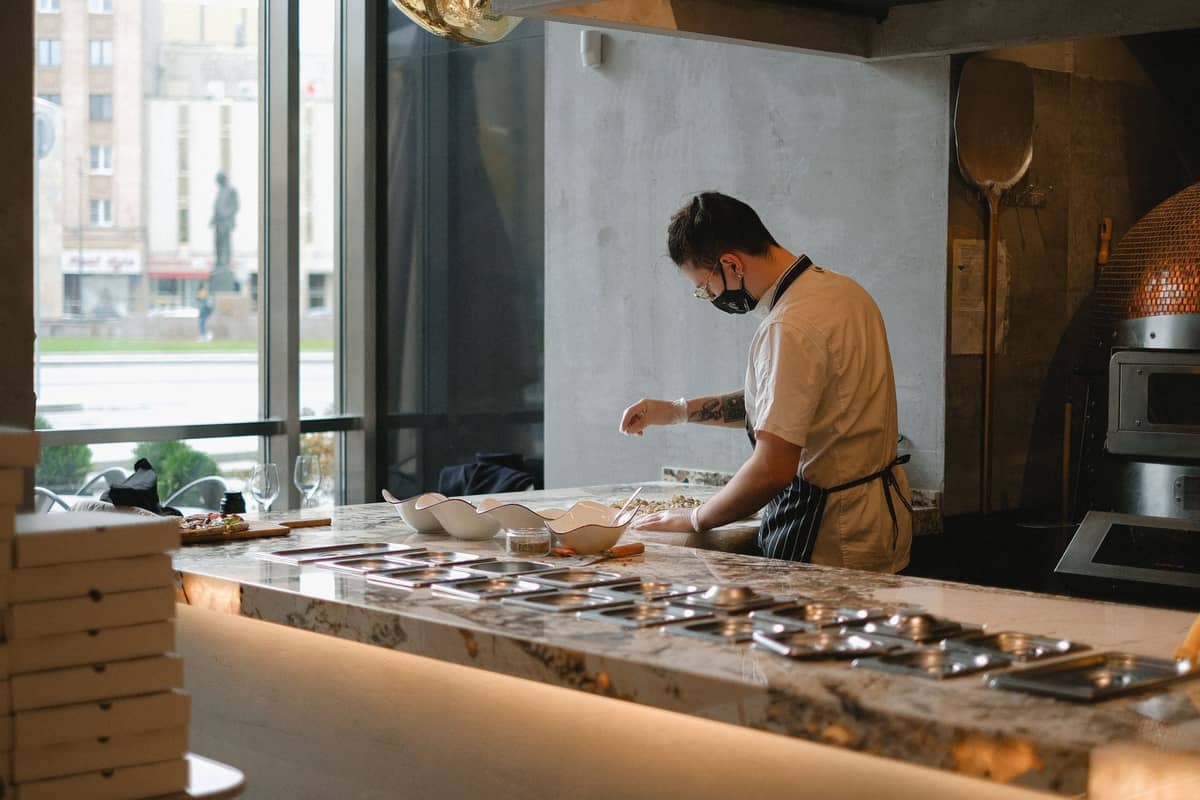 Chef en una cocina moderna de restaurante preparando comida cerca de una gran ventana con vistas a la ciudad de Varsovia