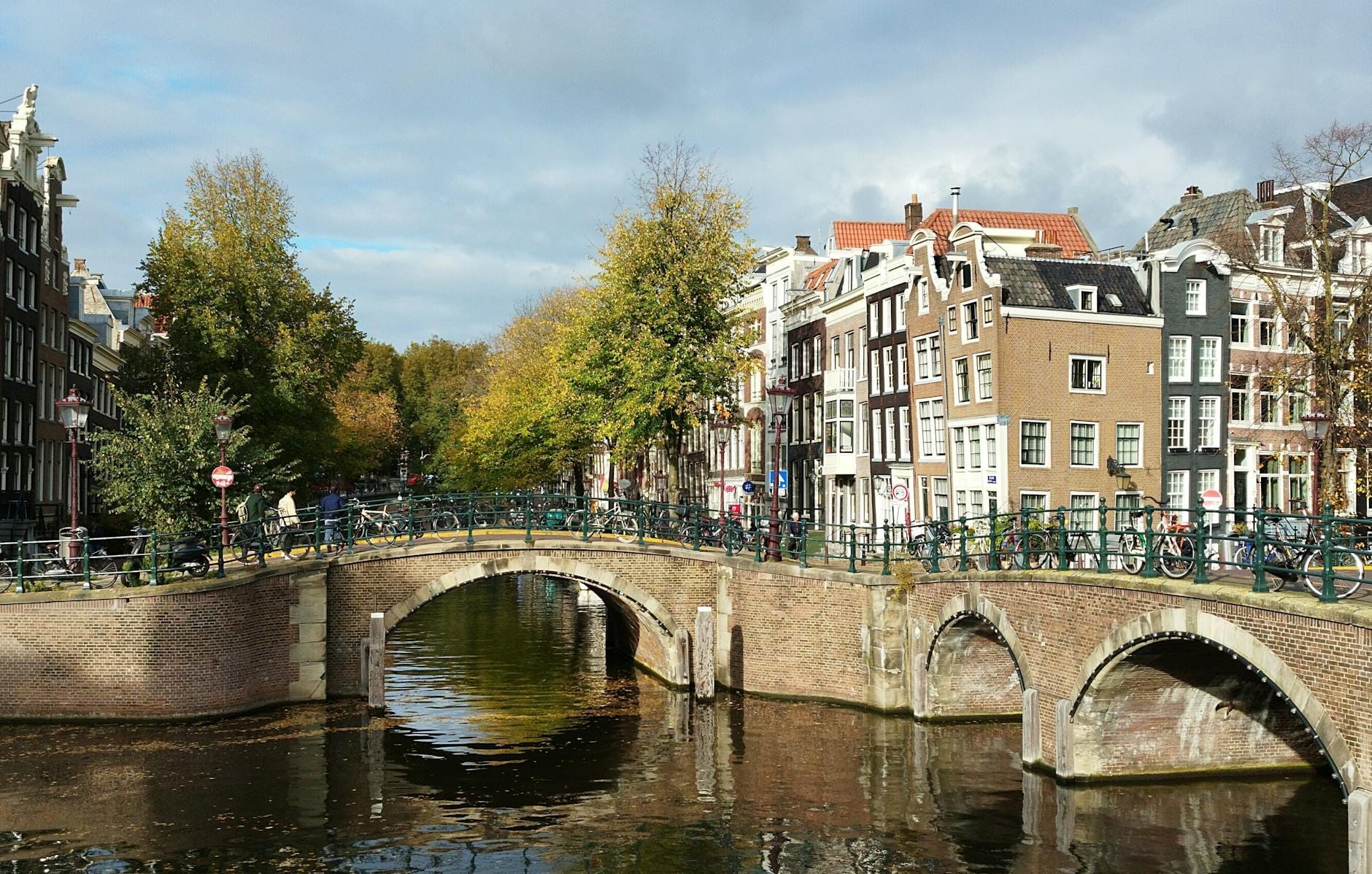 Escena clásica de canal en Ámsterdam con puentes arqueados, bicicletas y casas tradicionales estrechas a lo largo del agua.
