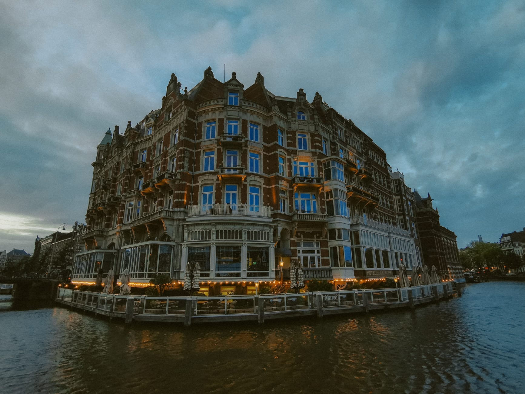 Gran hotel histórico con arquitectura ornamental a orillas de un canal de Ámsterdam, iluminado al atardecer con reflejos en el agua.