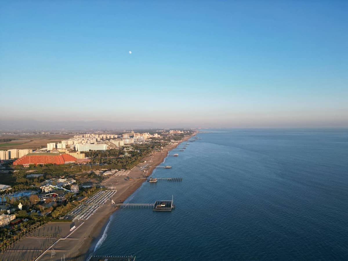 Aerial view of Lara Beach with a long sandy shoreline, clear calm water, and rows of large resort hotels along the coast.