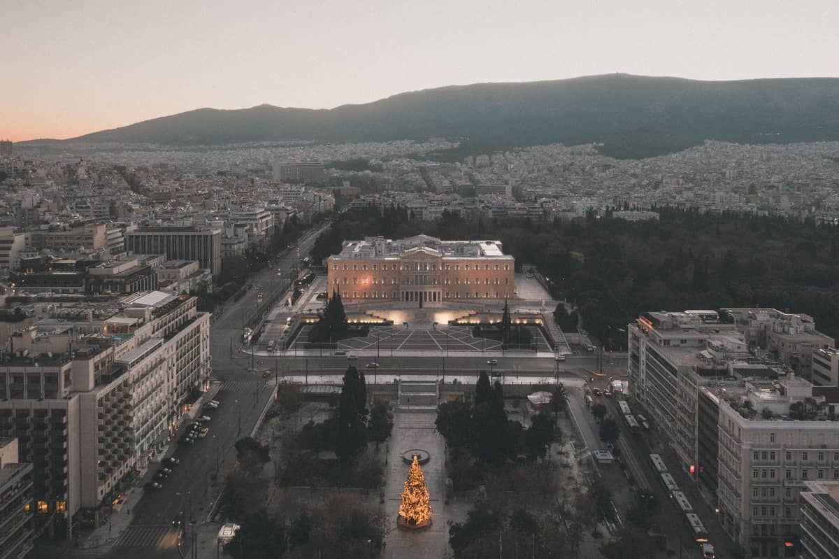 Pemandangan udara Lapangan Syntagma dengan gedung Parlemen Yunani dan lanskap kota di sekitarnya saat senja di pusat Athena.