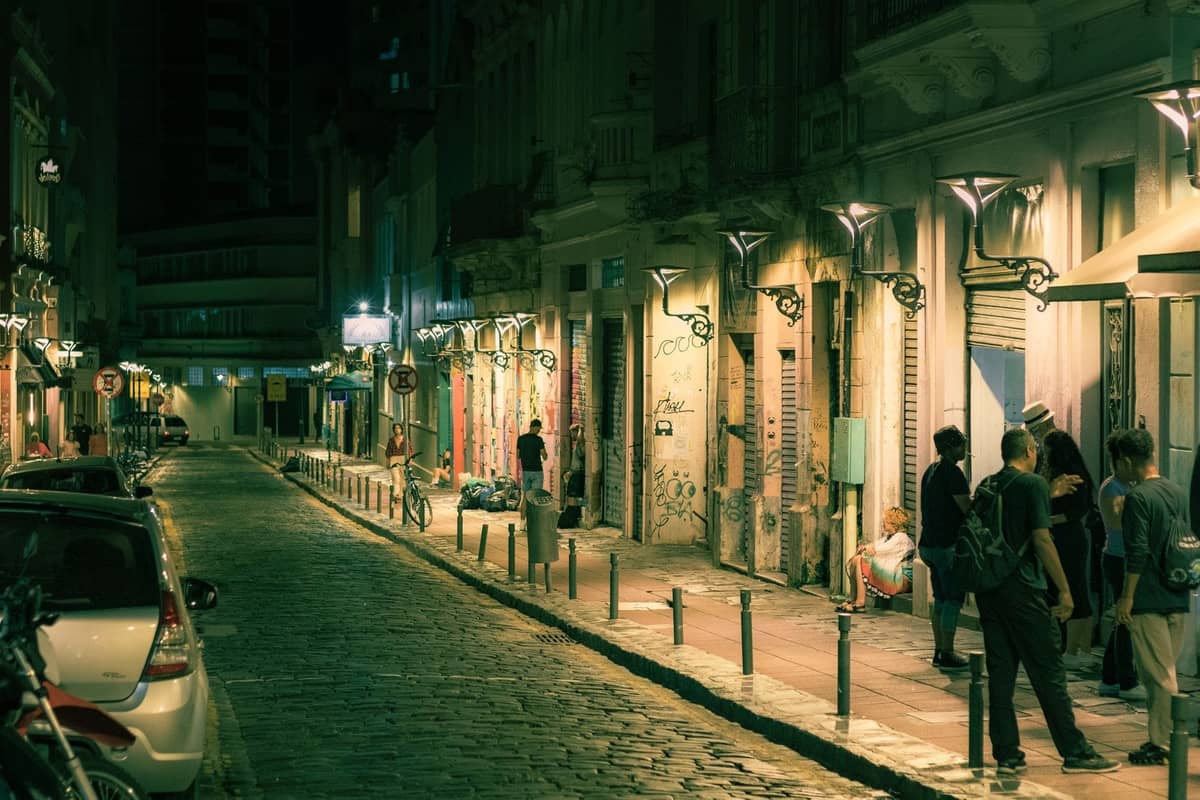 Pemandangan malam di jalan Athens yang ramai, dipenuhi toko-toko yang terang, grafiti, dan kelompok orang yang bercengkerama di trotoar.