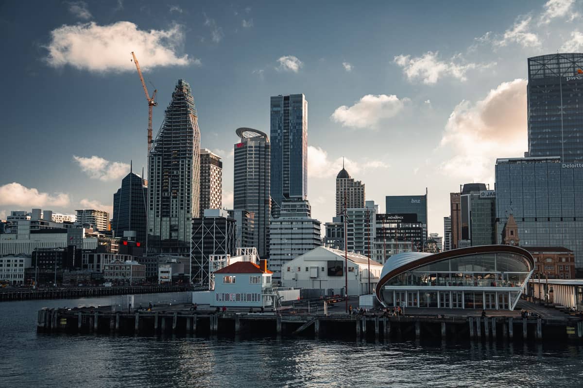 Waterfront des Auckland CBD mit modernen Wolkenkratzern, Hafengebäuden und dem Hafenwasser im Vordergrund unter blauem Himmel.