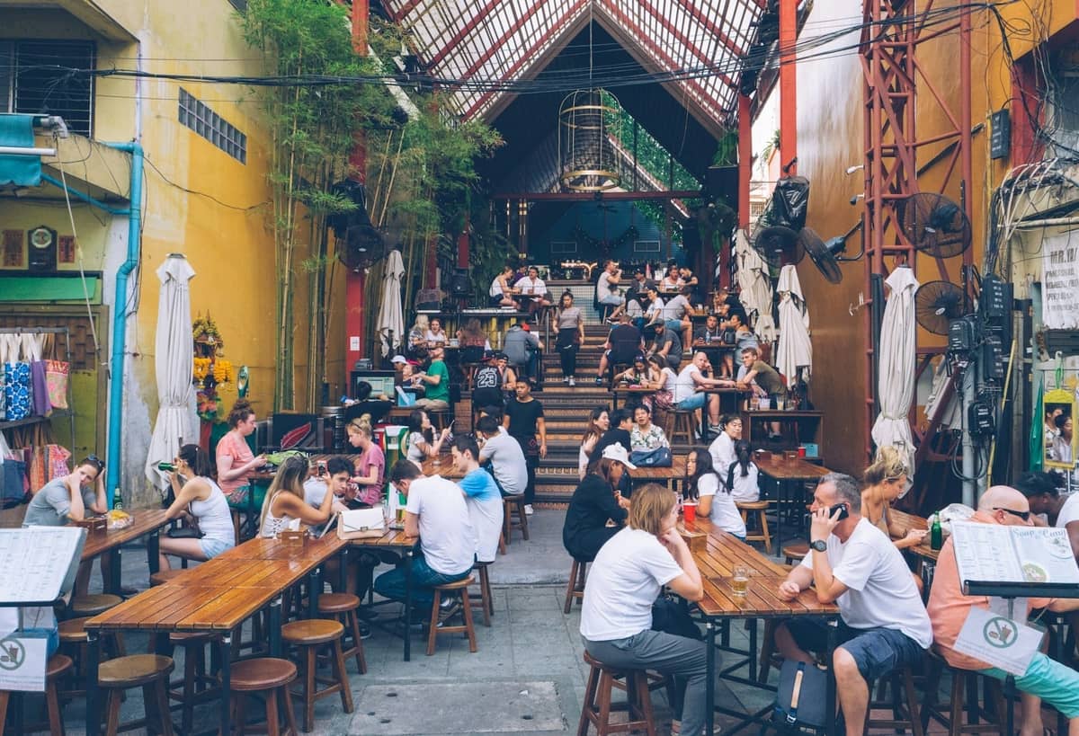 Cena na rua Khao San Road com mesas ao ar livre, restaurantes e mochileiros em Bangkok.