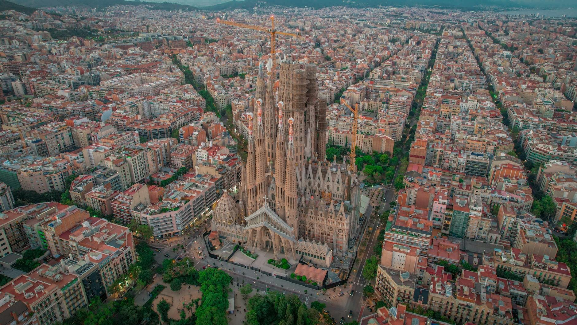 Aerial view of Barcelona’s Eixample district featuring the iconic Sagrada Familia surrounded by the distinctive grid of buildings and tree-lined streets.