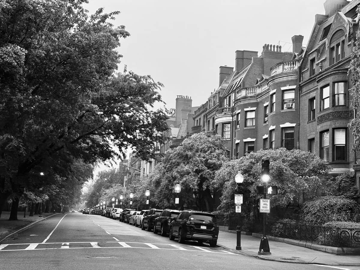 Schwarz-Weiß-Foto einer baumgesäumten Straße mit historischen Brownstone-Gebäuden und geparkten Autos, typisch für Bostons Back Bay.