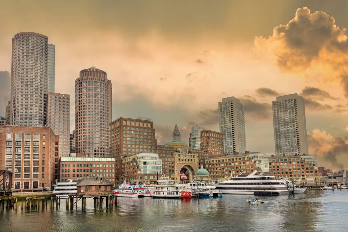 Skyline des Boston Seaport mit modernen Hochhäusern, Hafenhotels, Hafenblick und im Vordergrund festgemachten Booten im frühen Abendlicht.