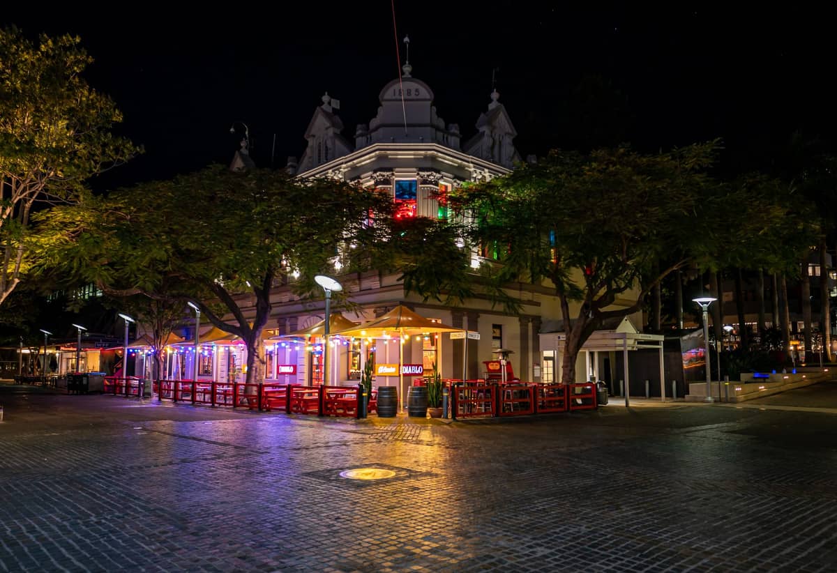 Night view of Fortitude Valley with a historic building, colorful lights, outdoor seating, and a lively street atmosphere.