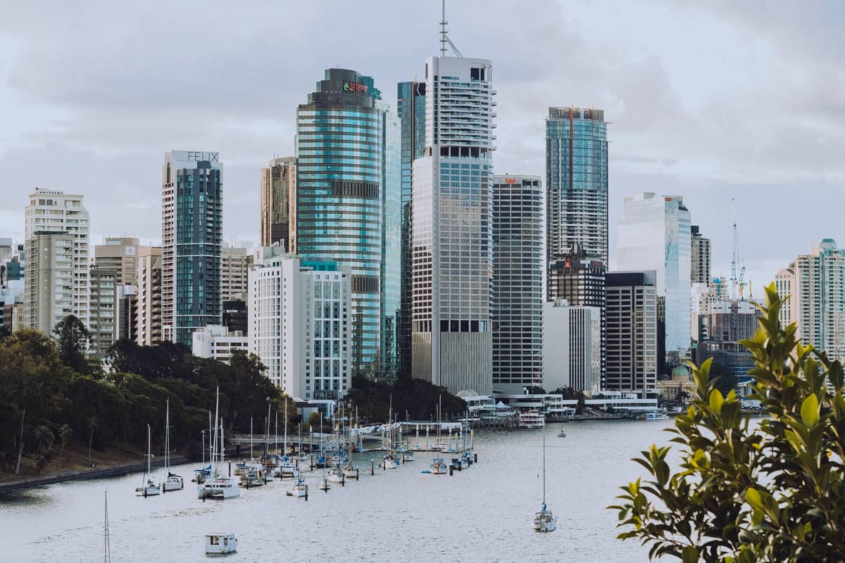 Panoramiczny widok na skyline Brisbane z wieżowcami i łodziami na rzece Brisbane na pierwszym planie, pod zachmurzonym niebem.