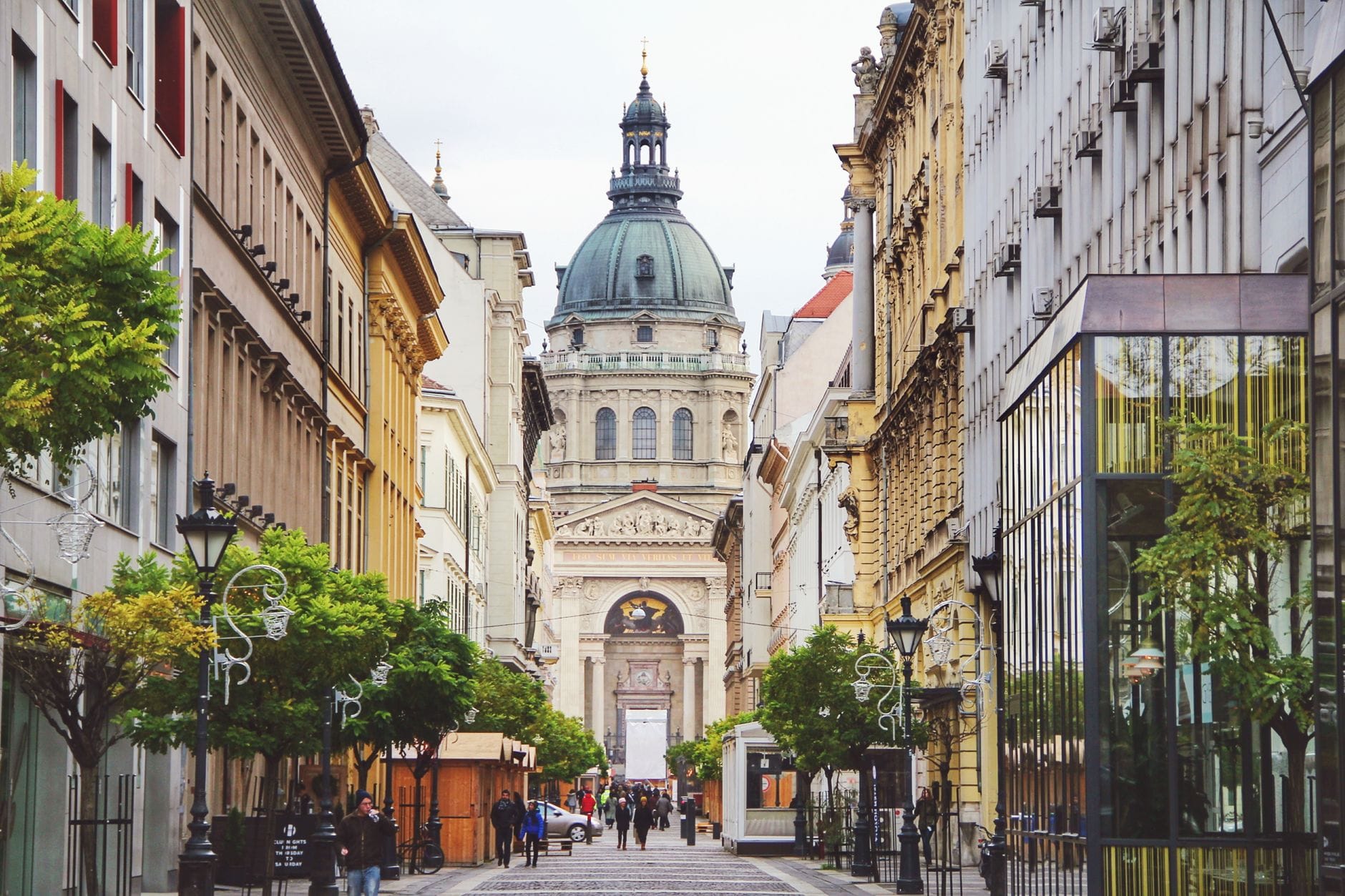 Fußgängerzone in der Budapester Innenstadt mit Passanten und Geschäften auf beiden Seiten, mit der Kuppel der Basilika St. Stephan im Hintergrund.