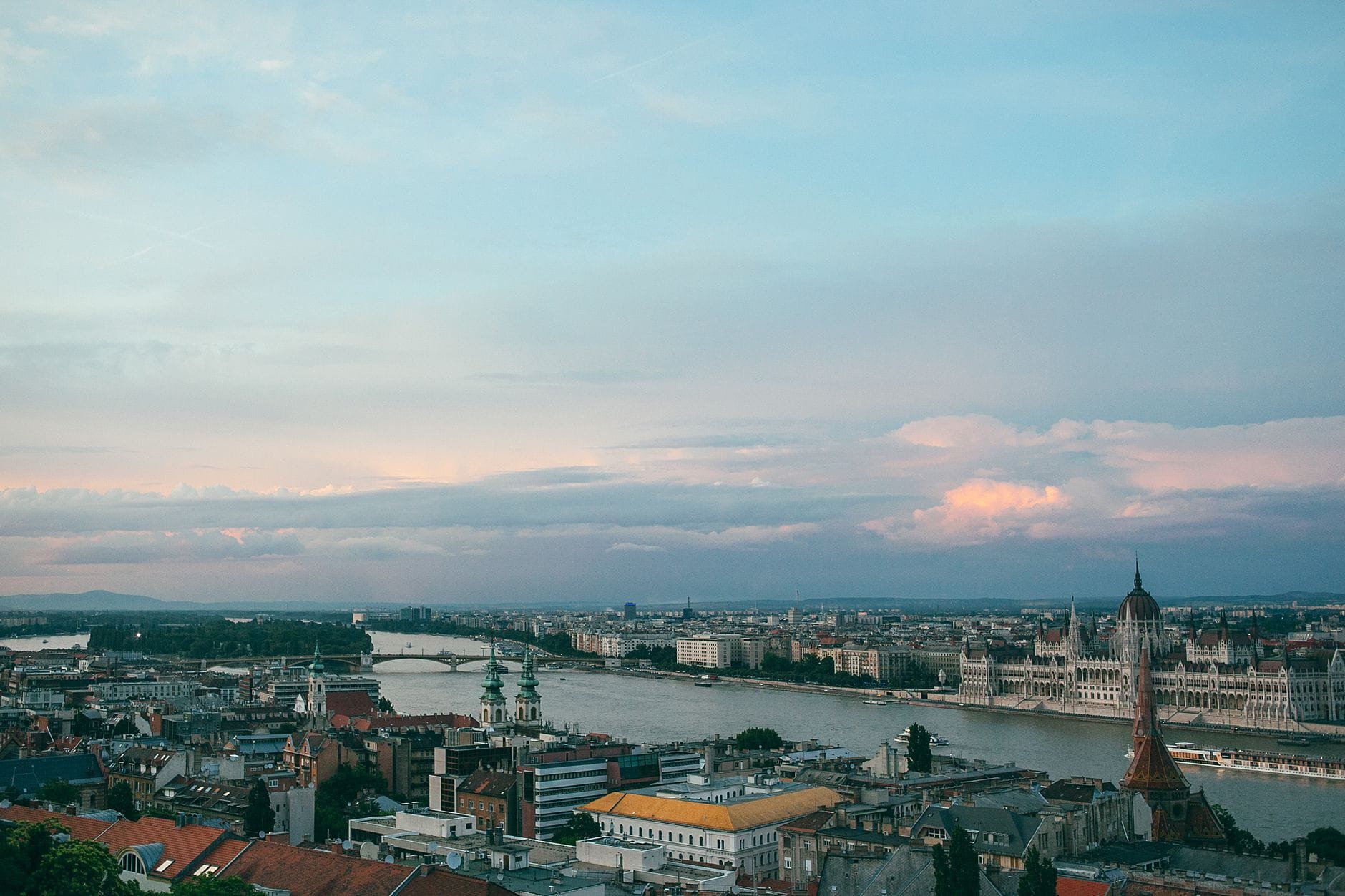 Weites Panorama von Budapest bei Sonnenuntergang mit Donau, Stadtsilhouette, historischen Gebäuden und dem Parlament – ein Überblick über die verschiedenen Stadtteile.