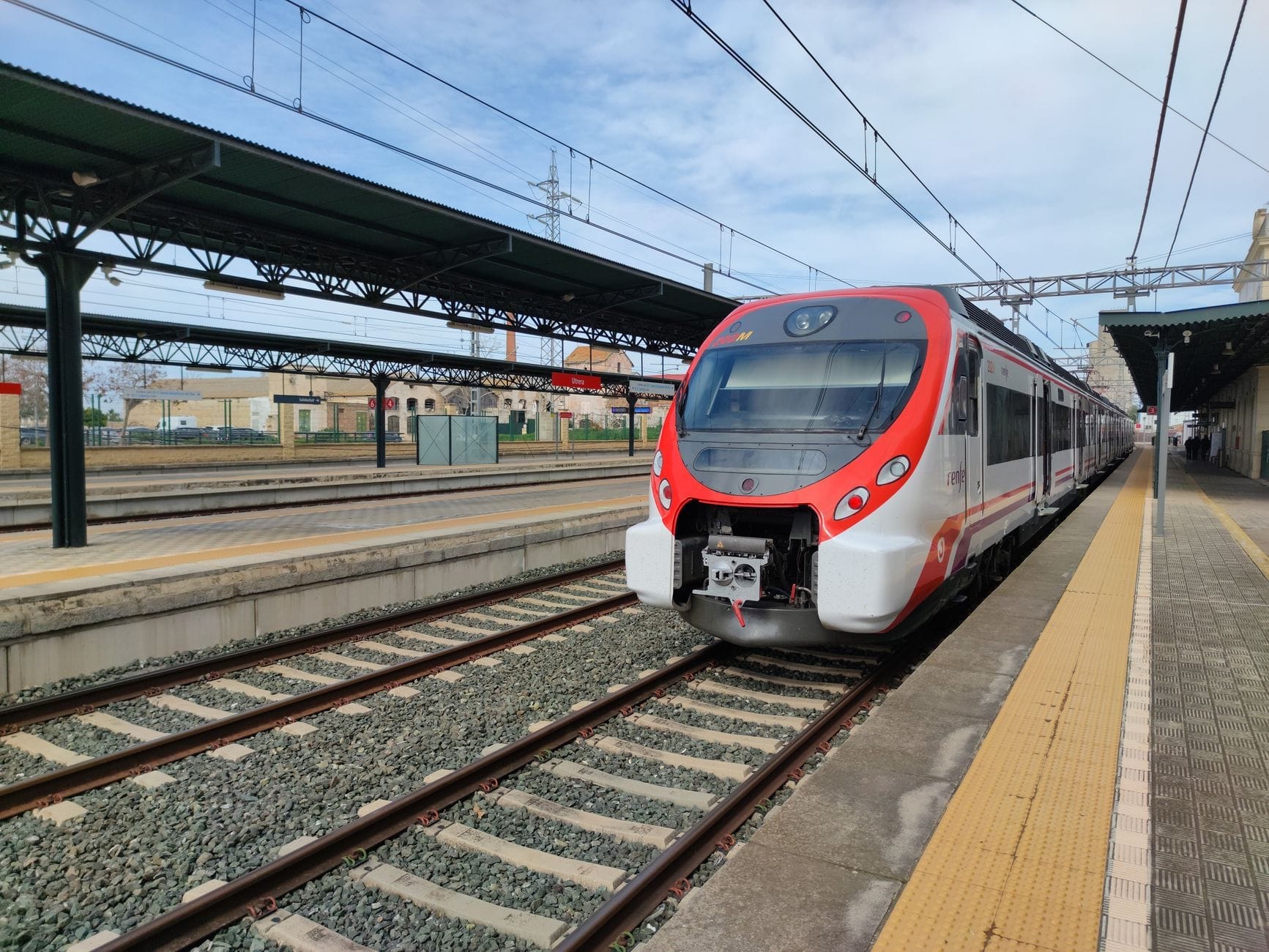 Modern regional train at a platform in a Spanish railway station on a sunny day, ready for boarding.