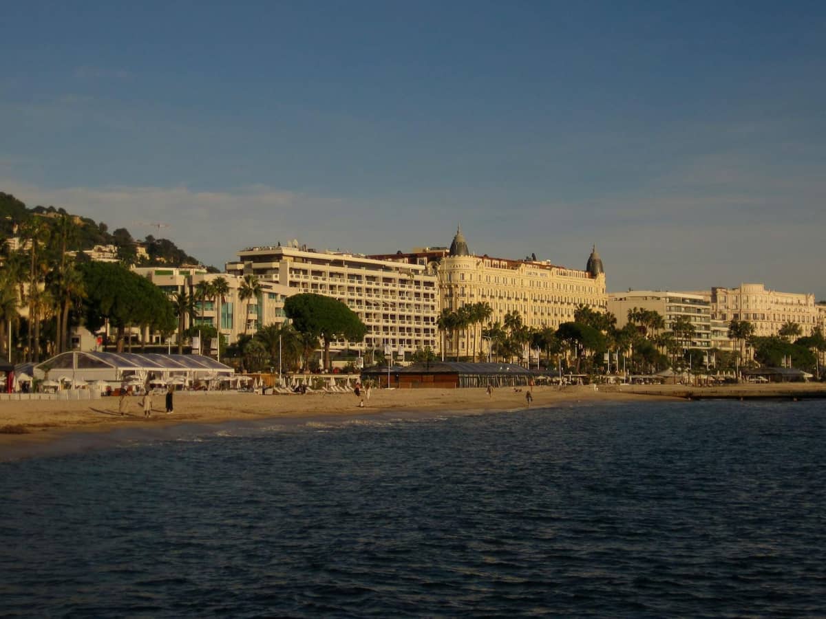 วิวจากทะเลของโรงแรมหรูริมชายหาดและต้นปาล์มตลอดแนวเลียบชายหาด La Croisette ในเมือง Cannes ยามอาทิตย์อัสดง
