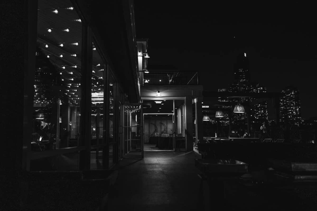 Schwarz-Weiß-Foto einer Dachbar oder eines Dachrestaurants bei Nacht mit Stadtlichtern im Hintergrund.