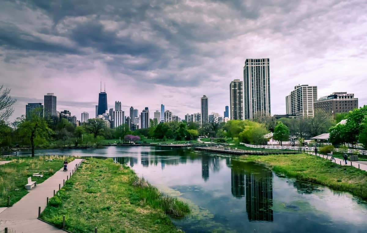 Skyline von Chicago hinter dem Teich und den Gehwegen des Lincoln Park unter einem dramatisch bewölkten Himmel, mit grüner Landschaft und Stadtbild im Zusammenspiel.