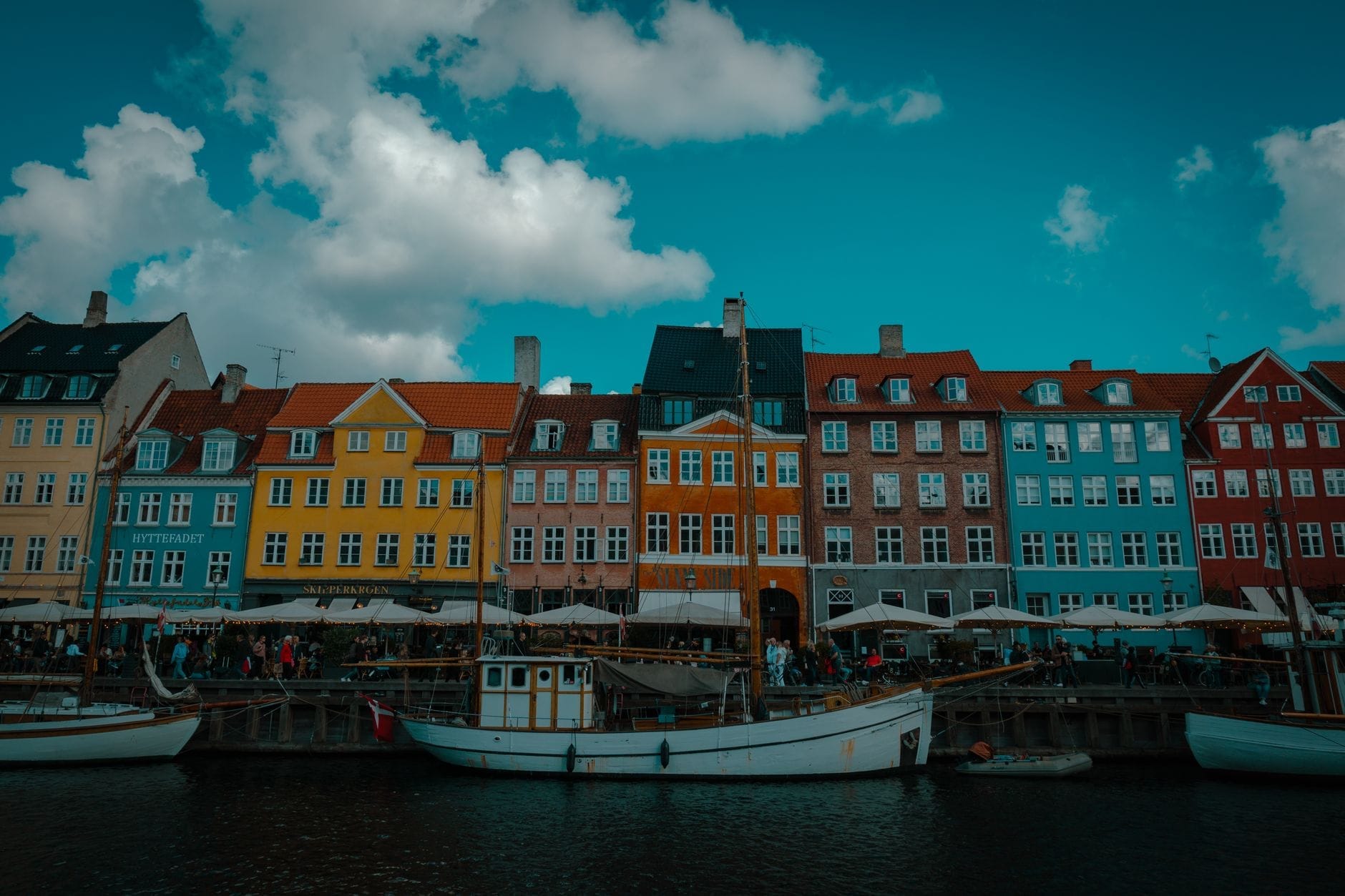 Prédios históricos e coloridos às margens do canal Nyhavn, em Copenhague, sob um céu azul com poucas nuvens, barcos ancorados na frente e uma energia contagiante perfeita para quem quer explorar a cidade.