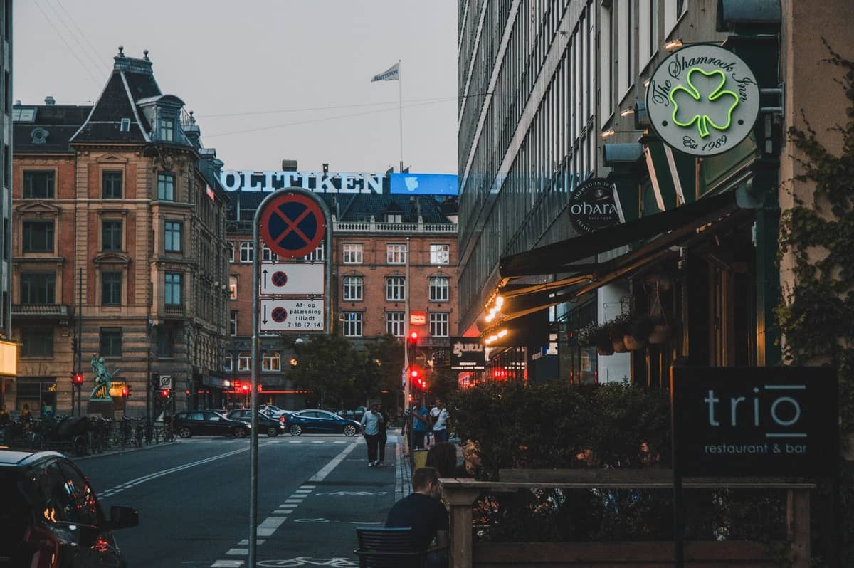 Abendliche Straßenszene im Vesterbro-Viertel in Kopenhagen mit Cafés, Leuchtreklamen, Fußgängern und historischen Gebäuden in der Nähe des Stadtzentrums.
