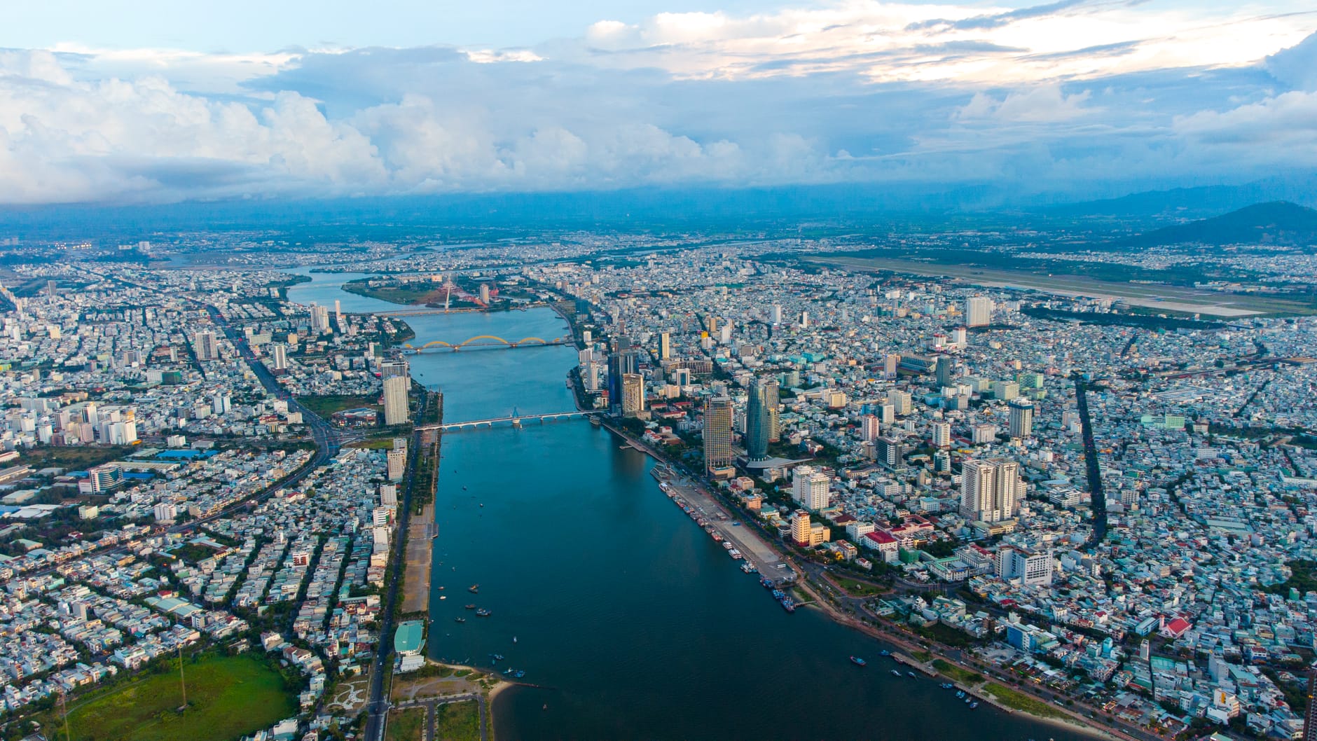 ภาพทางอากาศของเมืองดานังแสดงให้เห็นแม่น้ำฮาน หลายสะพาน และเขตชุมชนเมืองหลักพร้อมภูเขาเป็นฉากหลัง