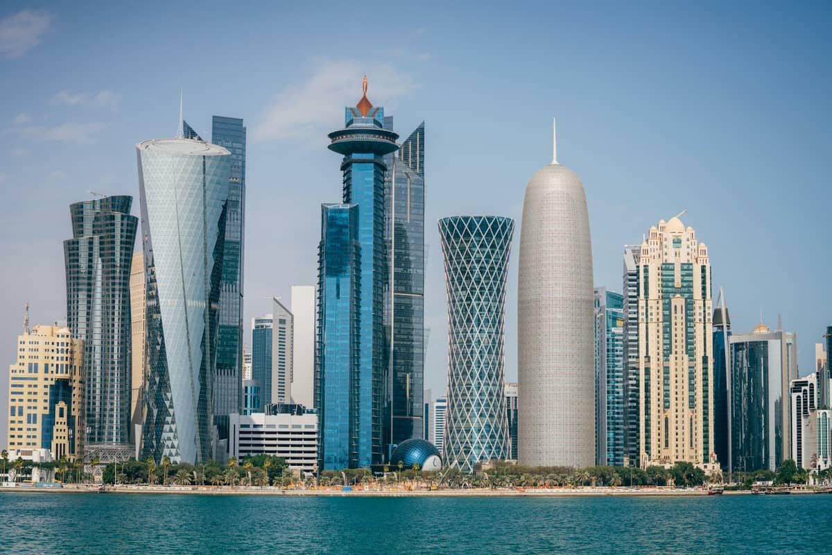 Beeindruckende Aussicht auf die Skyline von Dohas West Bay mit modernen Wolkenkratzern, vom Wasser aus unter strahlend blauem Himmel fotografiert.