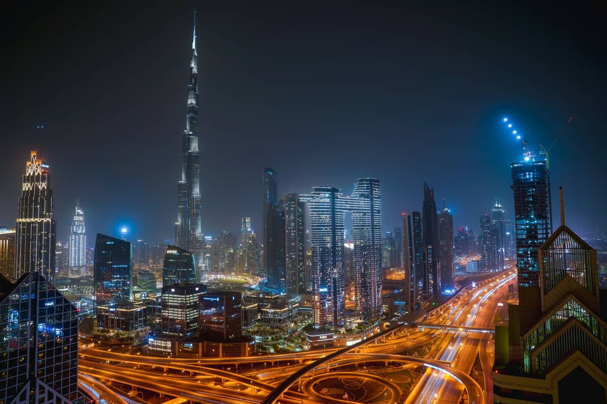 Nächtliche Skyline von Downtown Dubai mit dem Burj Khalifa, beleuchteten Wolkenkratzern und Highways mit Lichtspuren.
