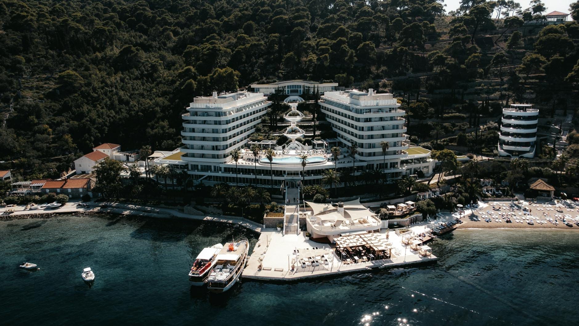 Vista aérea de un moderno hotel resort frente al mar con piscinas y acceso directo al mar, rodeado de exuberante vegetación en la costa de Dubrovnik.