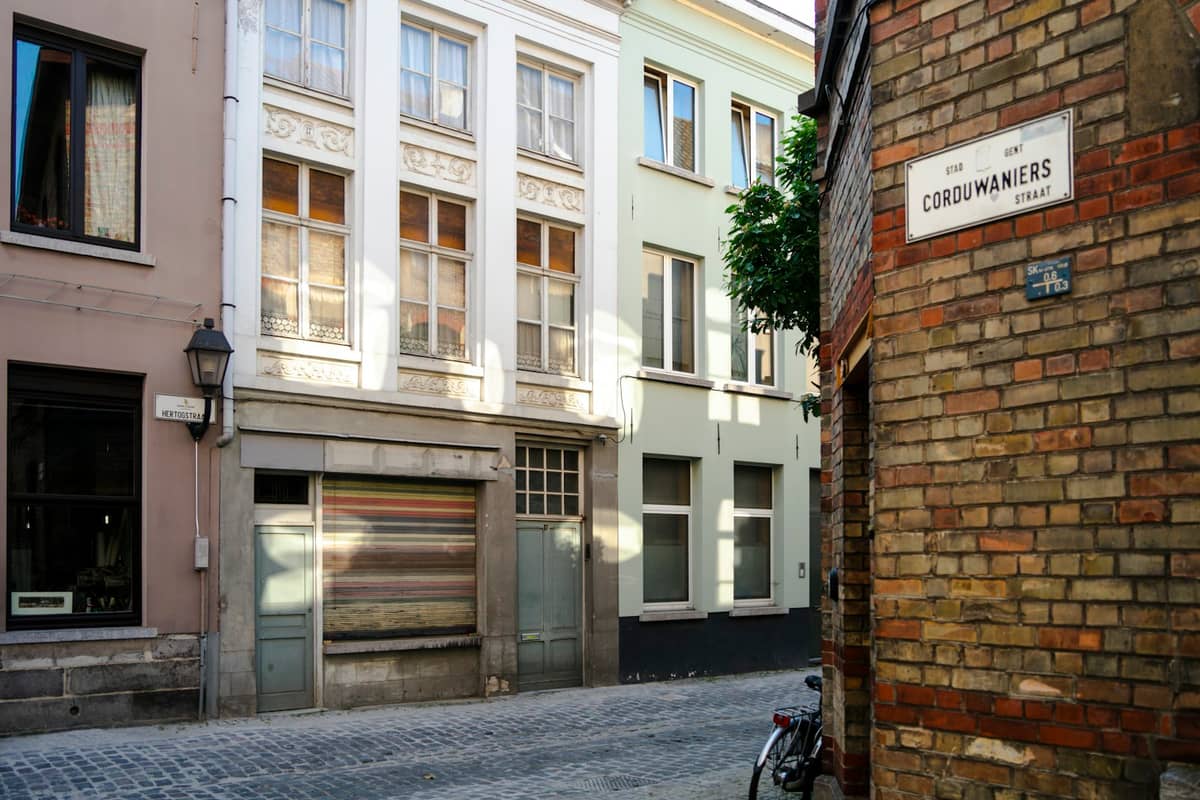A quiet cobbled street in Ghent’s Patershol neighborhood lined with historic buildings and a parked bicycle, with a street sign visible.