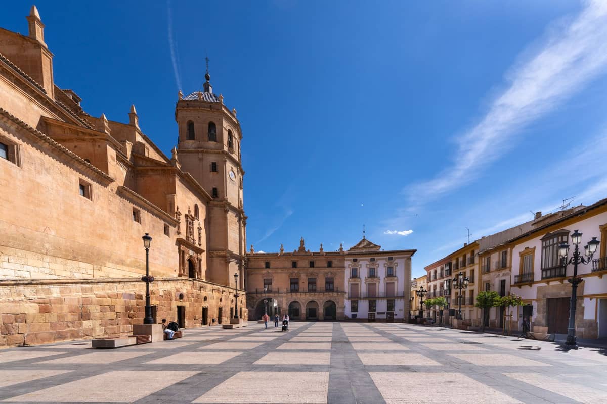 วิวกว้างของมหาวิหาร Granada และจัตุรัสใต้ท้องฟ้าสีฟ้า พร้อมผู้คนเดินอยู่ไม่กี่คนและอาคารประวัติศาสตร์ที่เรียงรายอยู่รอบลานกว้าง