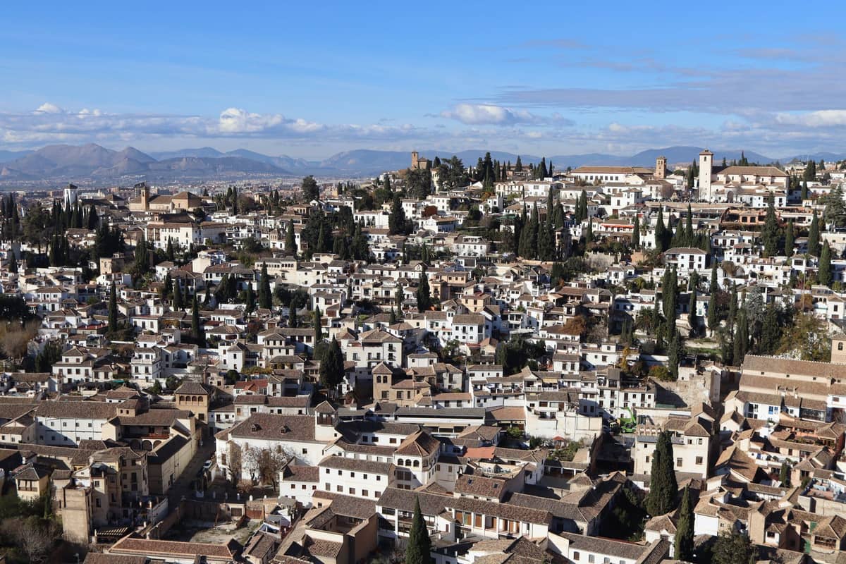 วิวภูมิทัศน์กว้างของย่าน Albaicín ในเมือง Granada พร้อมบ้านทาสีขาว ถนนแคบ และต้นไซเปรสภายใต้ท้องฟ้าสีฟ้าสดใส