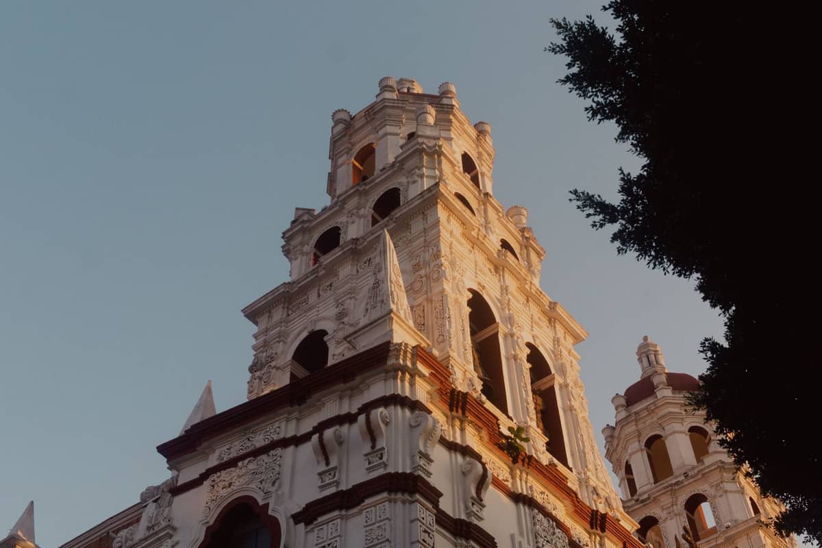 Untersicht des verzierten Glockenturms einer historischen Kirche im Centro Histórico von Guadalajara, mit Bäumen, die das Gebäude teilweise einrahmen.