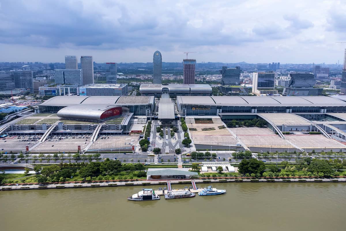 Aerial view of the Canton Fair Complex in Pazhou, Guangzhou, with modern exhibition halls, nearby skyscrapers, and the river in the foreground.