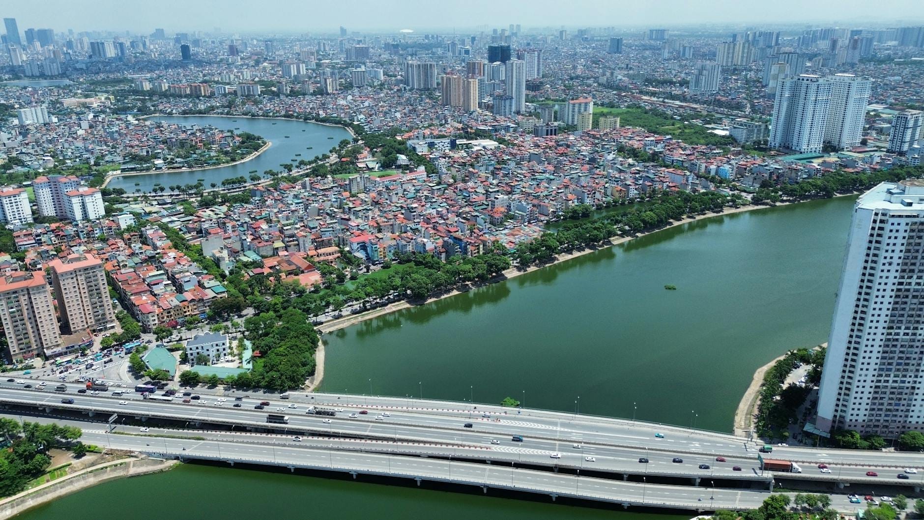 Aerial view of Hanoi showing distinct neighborhoods, lakes, high-rise and low-rise buildings, and major roads dividing districts.