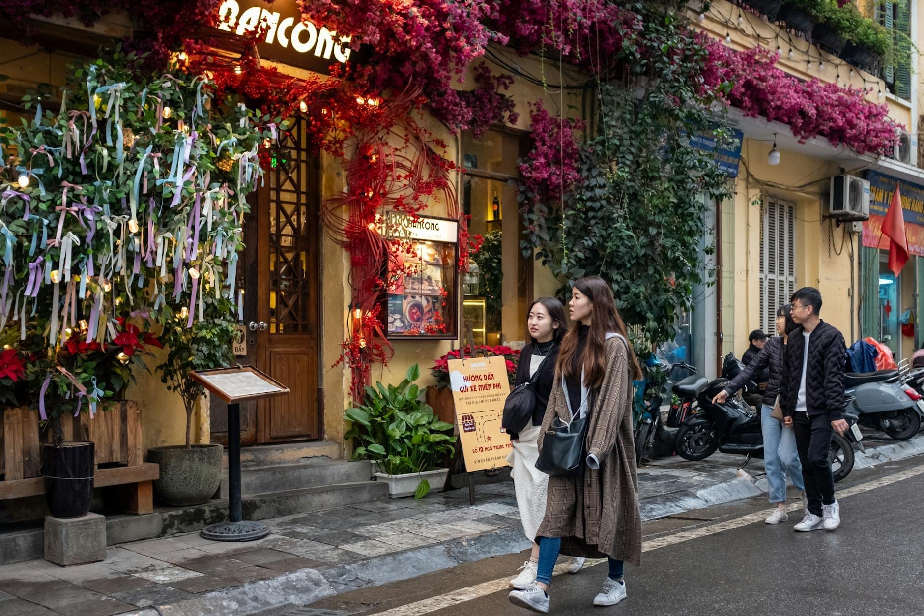 People walking along a lively Hanoi street with colorful flowers and vibrant local businesses, showcasing the atmosphere and charm of Hanoi’s neighborhoods.