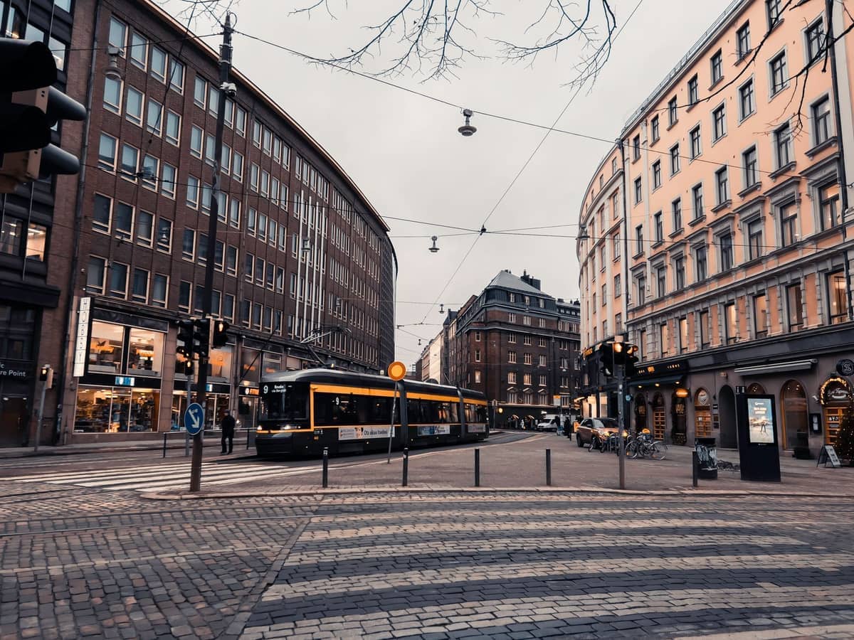 Eléctrico amarelo a passar por uma rua central de Helsínquia ladeada de edifícios históricos e lojas num dia nublado.