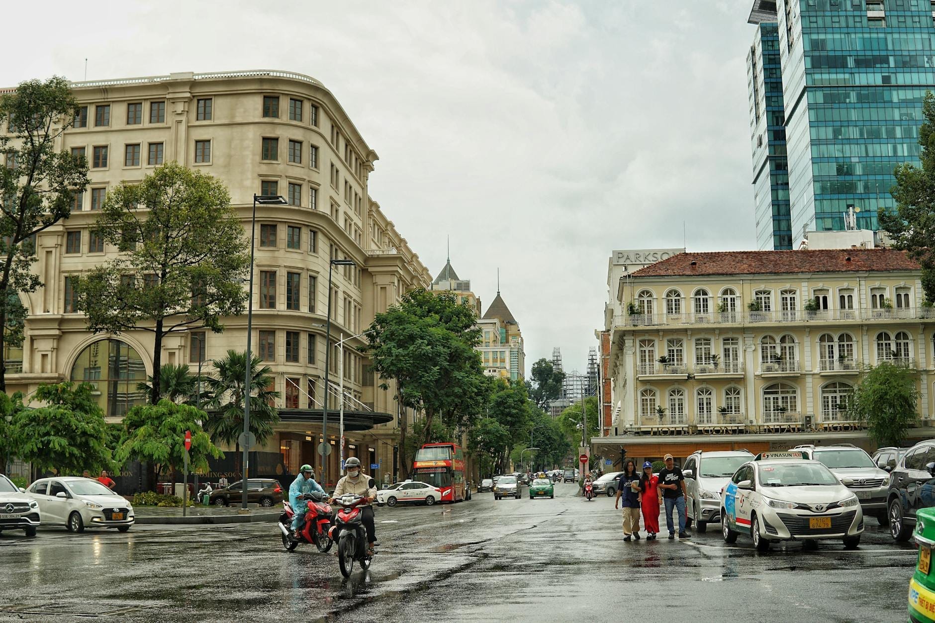 Đường phố trung tâm tại Quận 1, Thành phố Hồ Chí Minh với các tòa nhà thời thuộc địa, cây xanh, ô tô, xe máy và người đi bộ trong một ngày mưa.