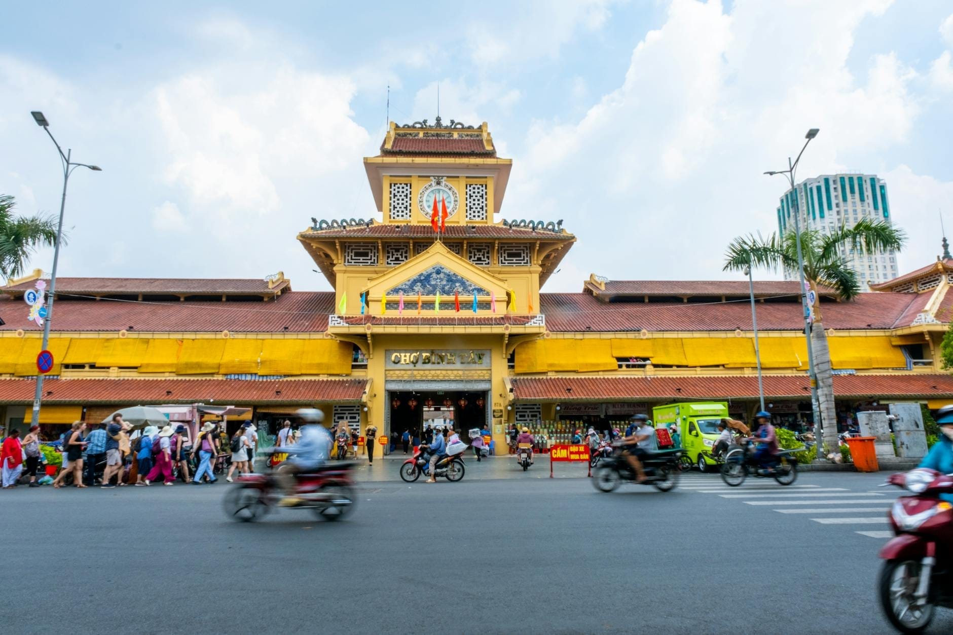 Góc nhìn rộng của tòa nhà chợ Bình Tây màu vàng lộng lẫy, nhộn nhịp người và xe máy bên ngoài ở khu vực Chợ Lớn, Thành phố Hồ Chí Minh.