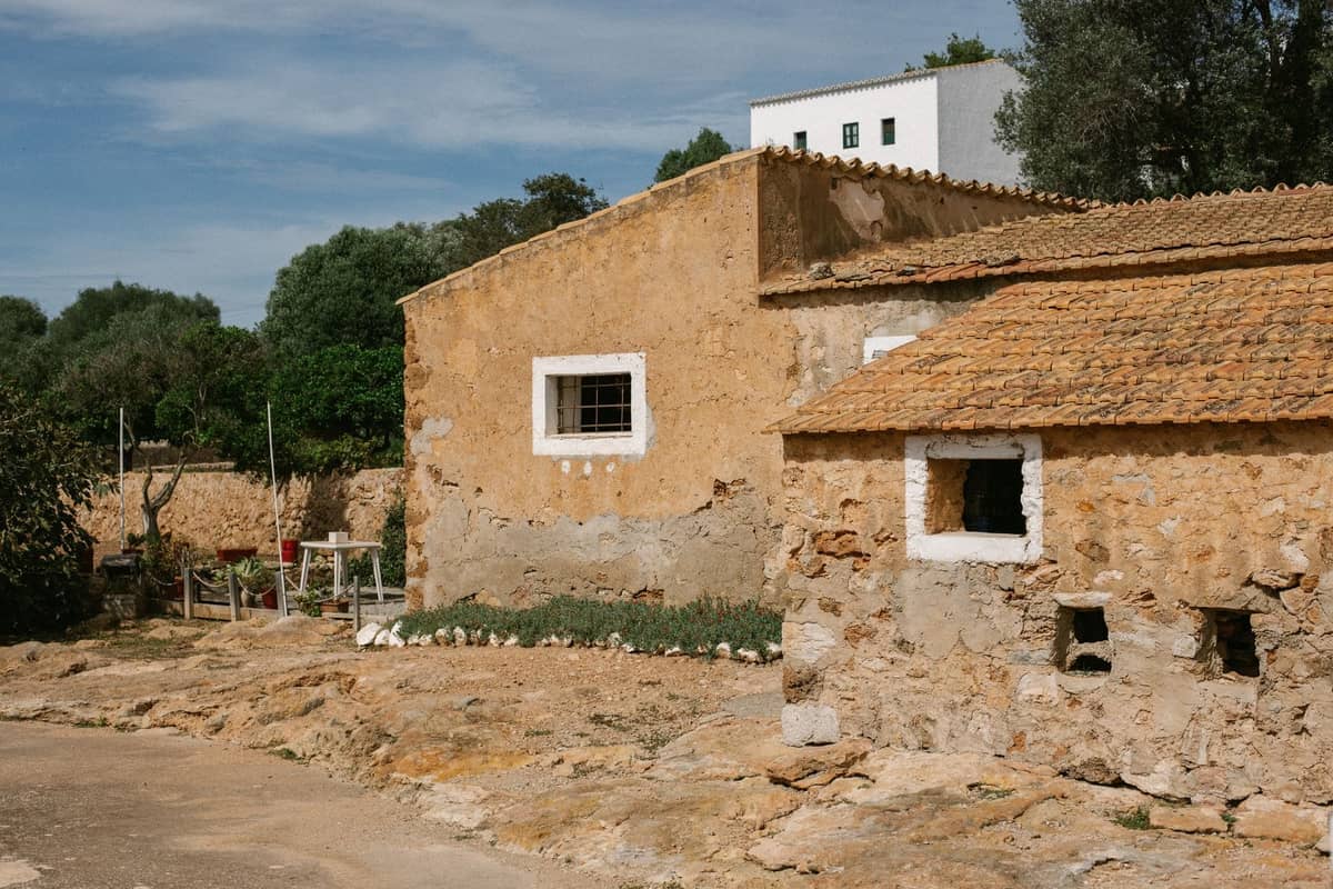 Traditional rural stone and clay farm building surrounded by dry earth and greenery in the countryside of Ibiza’s north.