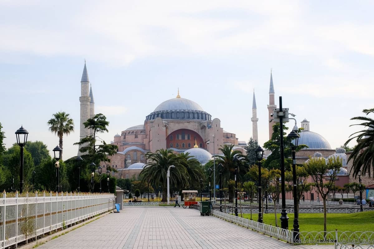Vista diurna de la Hagia Sophia en Sultanahmet, Estambul, vista desde un camino peatonal bordeado de palmeras y farolas.