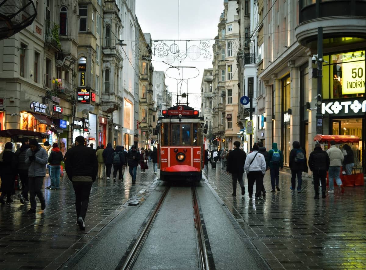 Vista de la avenida Istiklal de Estambul en Beyoğlu con el icónico tranvía rojo, peatones, tiendas y edificios históricos en un día lluvioso.