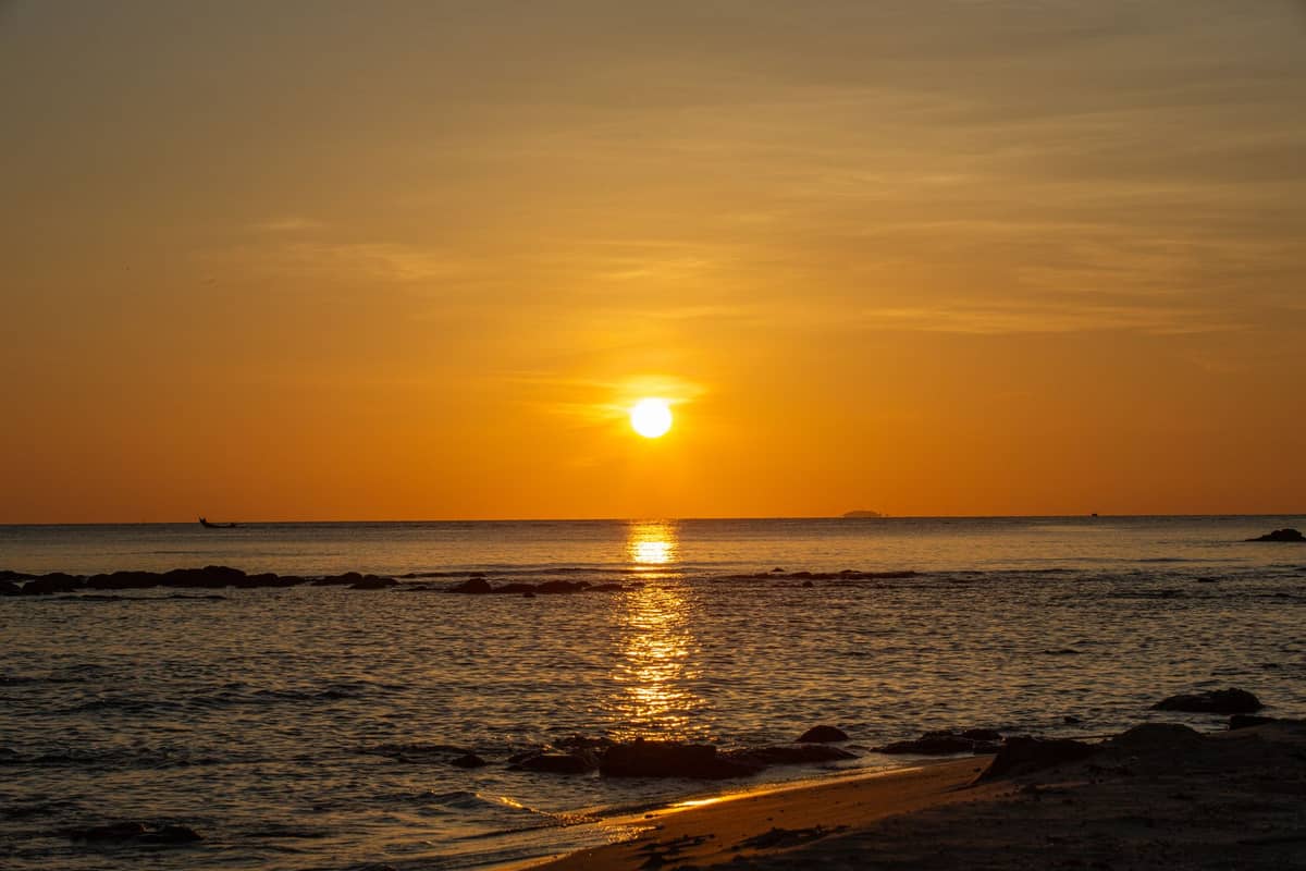 Coucher de soleil doré sur une plage calme avec des vagues douces et des rochers épars sur le rivage.