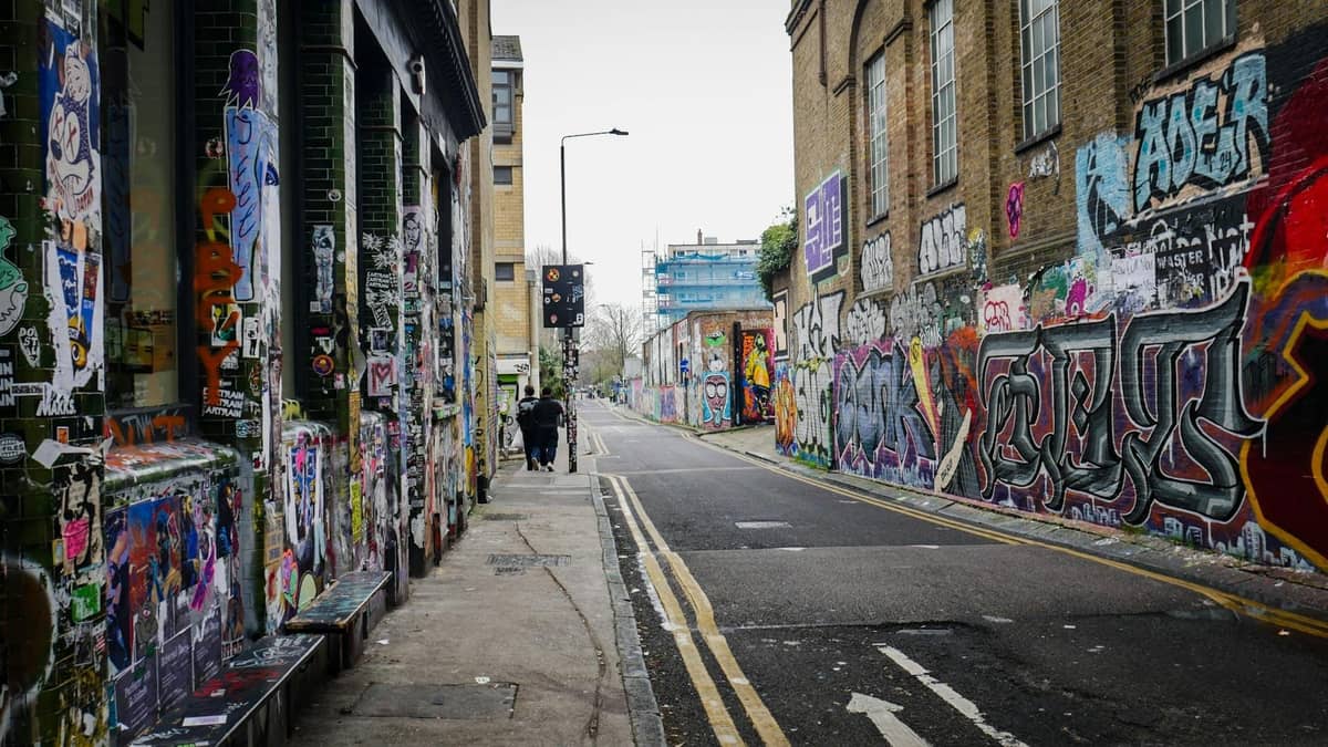 Rua em Shoreditch, East London, ladeada por grafites vibrantes em ambos os lados e algumas pessoas caminhando