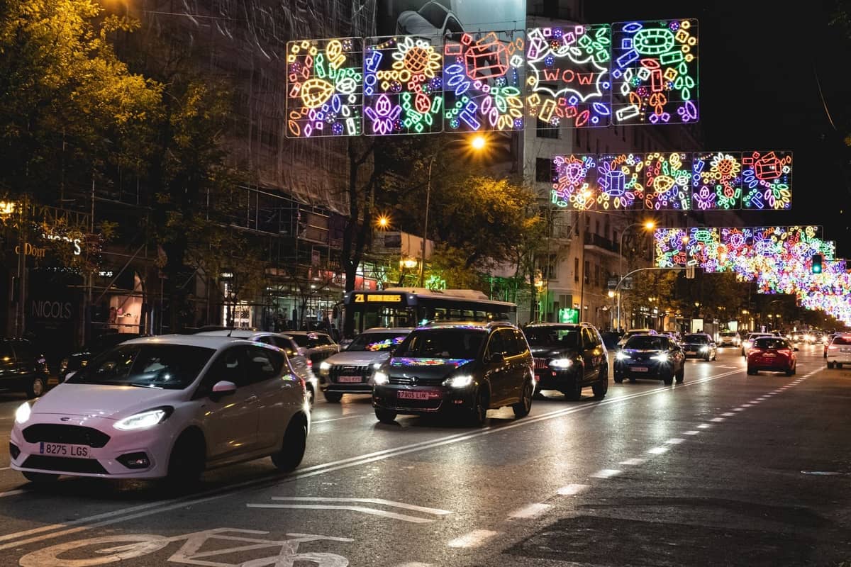 Belebte Straße in Madrid bei Nacht mit bunten Neonlichtern, vorbeifahrenden Autos und lebhafter Stadtenergie.