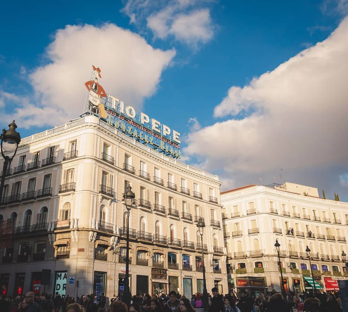 Belebter Platz in Madrid mit dem ikonischen Tio Pepe Schild an einem historischen Gebäude unter blauem Himmel